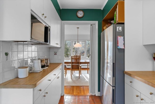 kitchen with light countertops, hanging light fixtures, decorative backsplash, freestanding refrigerator, and white cabinetry