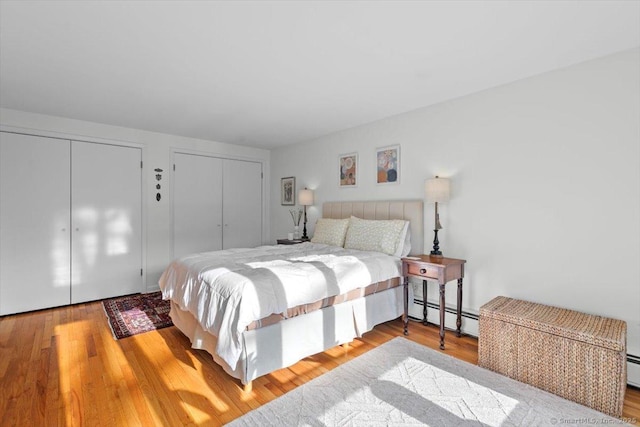 bedroom featuring light wood-style flooring, baseboard heating, and two closets