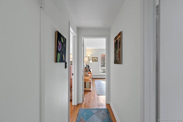 hall with a baseboard radiator, baseboards, and light wood finished floors