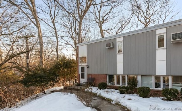 view of snow covered exterior with brick siding and a wall mounted AC