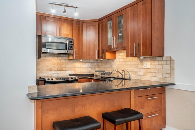 kitchen with brown cabinetry, glass insert cabinets, a breakfast bar, stainless steel appliances, and a sink