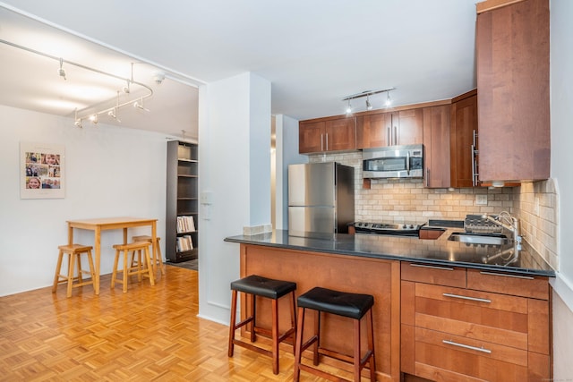 kitchen with a sink, appliances with stainless steel finishes, brown cabinets, decorative backsplash, and dark countertops