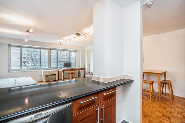 kitchen featuring dishwashing machine, a wall unit AC, brown cabinetry, dark countertops, and rail lighting