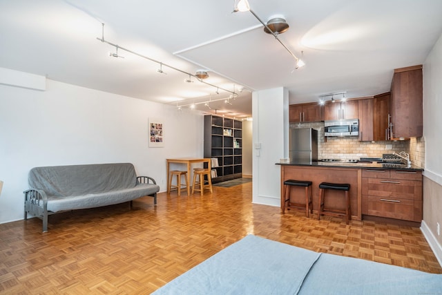 kitchen with brown cabinets, dark countertops, backsplash, appliances with stainless steel finishes, and open floor plan