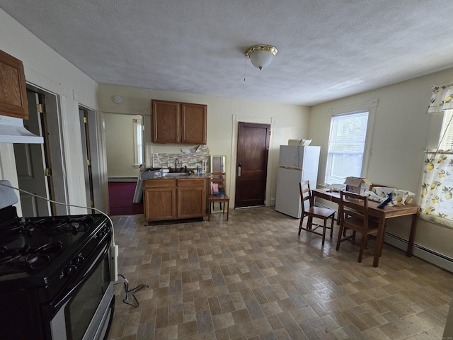 kitchen with brown cabinetry, gas range, freestanding refrigerator, under cabinet range hood, and a sink