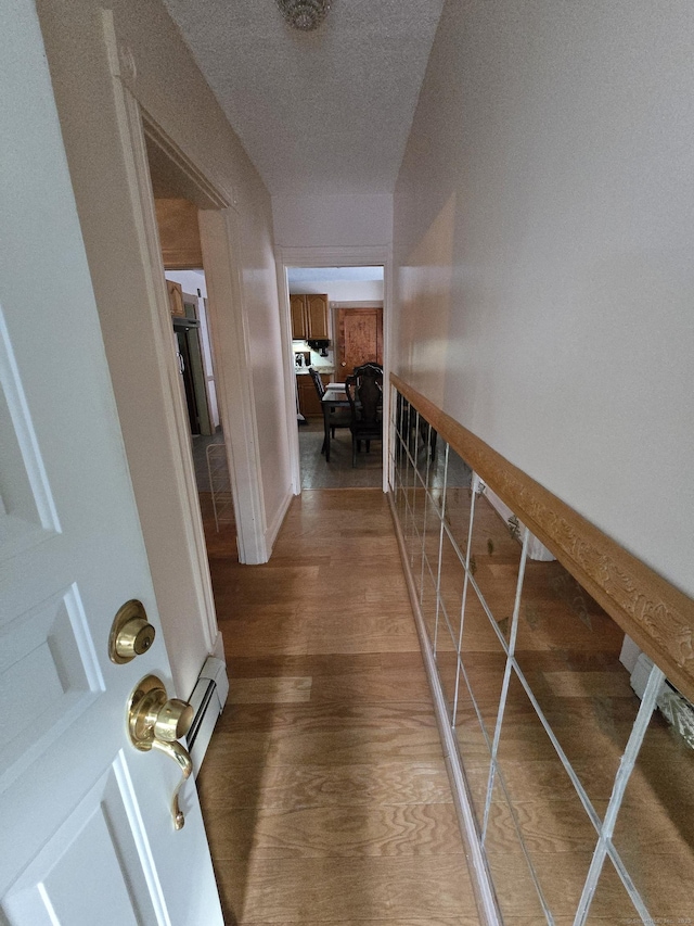 hall with a baseboard heating unit, a textured ceiling, baseboards, and wood finished floors