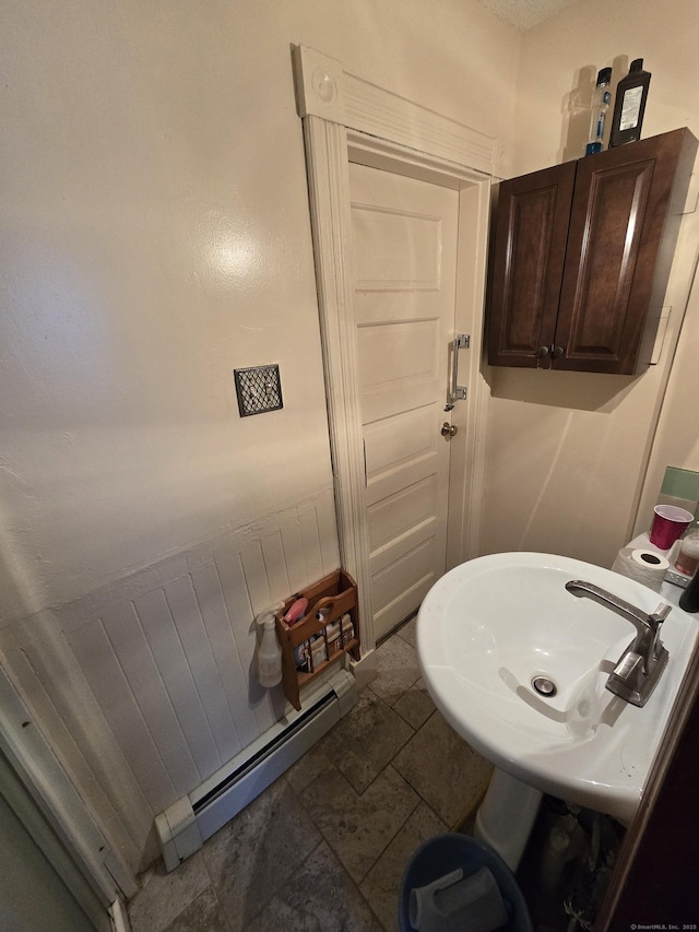 bathroom featuring a baseboard radiator, stone finish floor, and a sink