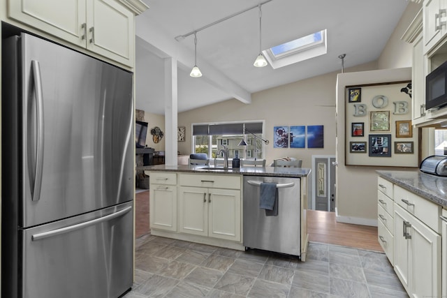 kitchen featuring a sink, appliances with stainless steel finishes, dark stone counters, lofted ceiling with skylight, and decorative light fixtures