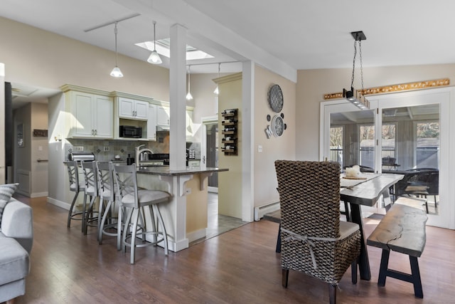 kitchen with black microwave, a baseboard radiator, a peninsula, a kitchen breakfast bar, and lofted ceiling with skylight