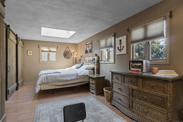 bedroom with light wood finished floors, a barn door, a textured ceiling, and a skylight