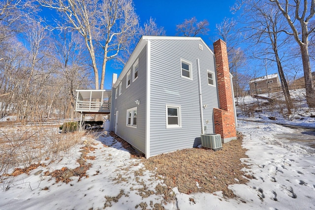 view of snow covered exterior with a chimney and central AC unit