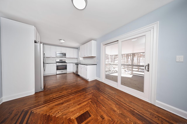 kitchen with baseboards, decorative backsplash, dark countertops, stainless steel appliances, and white cabinetry