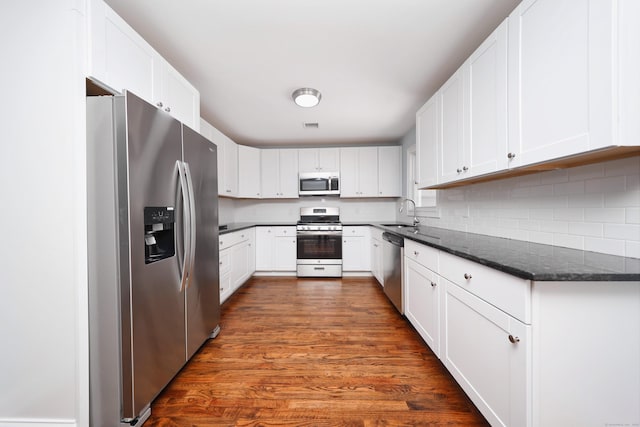 kitchen with white cabinets, dark stone counters, dark wood-style flooring, stainless steel appliances, and a sink