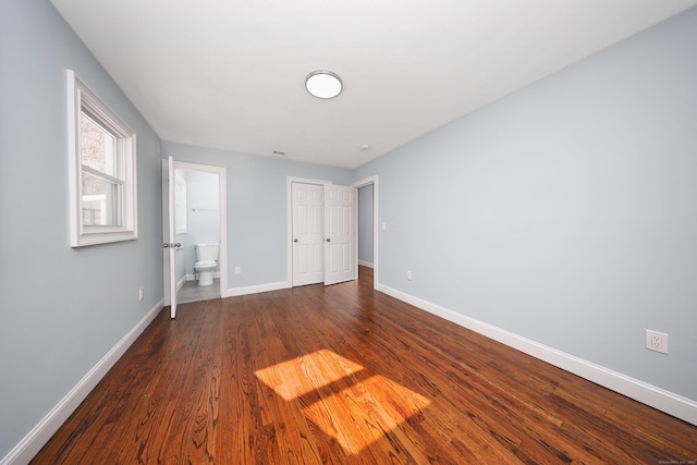 unfurnished bedroom with ensuite bath, dark wood-style flooring, a closet, and baseboards