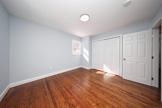 unfurnished bedroom featuring dark wood-type flooring, a closet, and baseboards