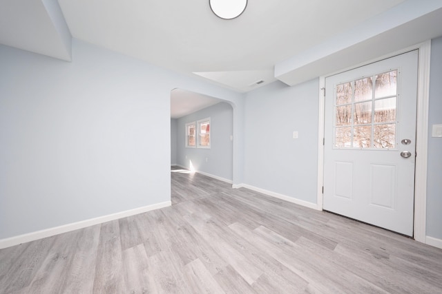 foyer entrance with arched walkways, light wood-style flooring, and baseboards