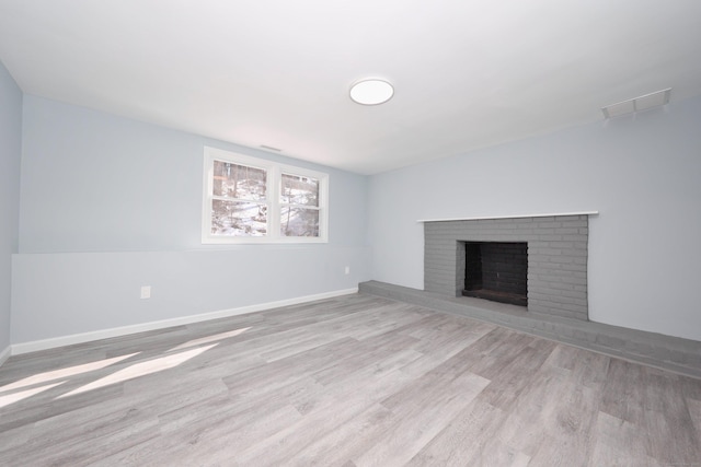 unfurnished living room with light wood-type flooring, a brick fireplace, visible vents, and baseboards