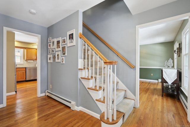 stairs featuring wood-type flooring, a baseboard heating unit, and baseboards