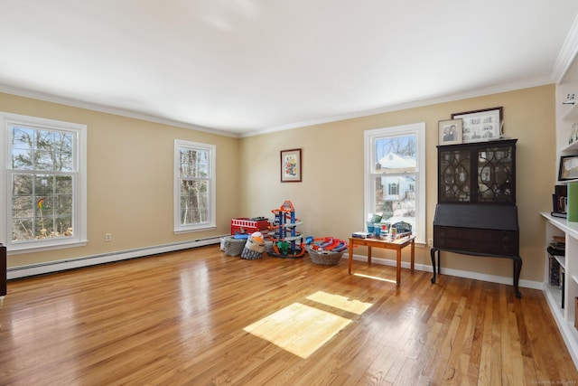 playroom featuring a baseboard heating unit, wood-type flooring, ornamental molding, and baseboards