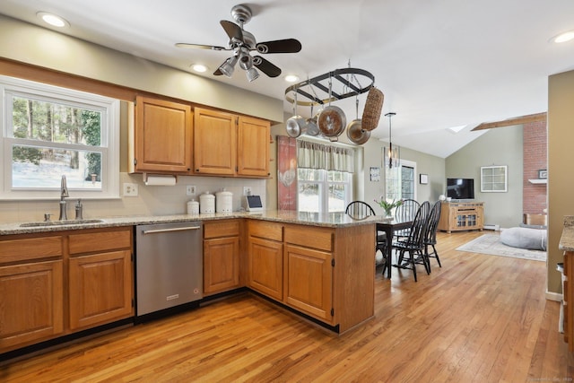 kitchen featuring a peninsula, stainless steel dishwasher, light stone counters, and a healthy amount of sunlight