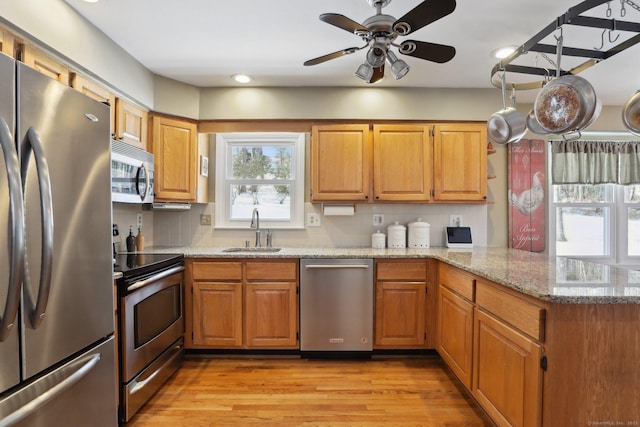 kitchen featuring light wood finished floors, appliances with stainless steel finishes, a peninsula, light stone countertops, and a sink