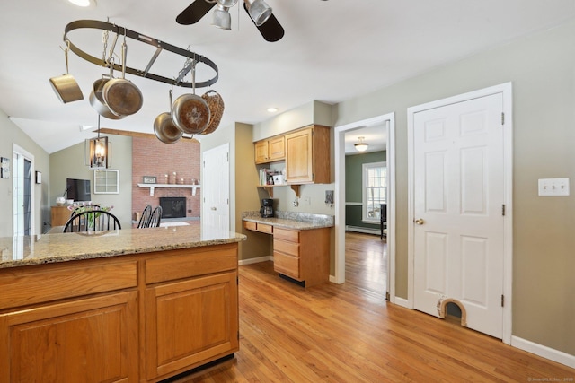 kitchen with light stone countertops, light wood-style floors, a brick fireplace, and a ceiling fan