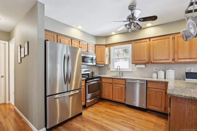 kitchen with stainless steel appliances, a sink, backsplash, light stone countertops, and light wood finished floors