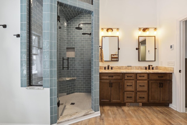 full bathroom with double vanity, a shower stall, a sink, and wood finished floors