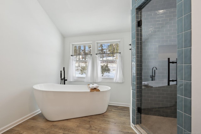 bathroom featuring vaulted ceiling, a freestanding tub, wood finished floors, and a shower stall