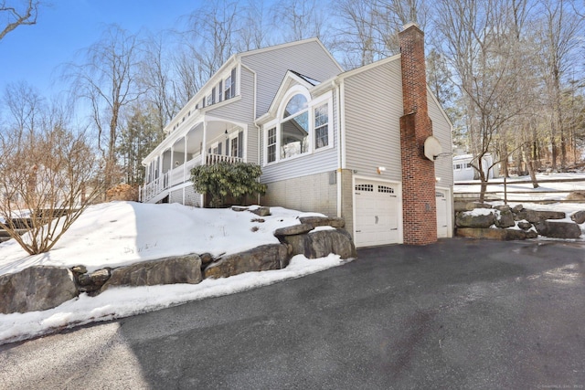 view of snow covered exterior with a garage, a chimney, and aphalt driveway