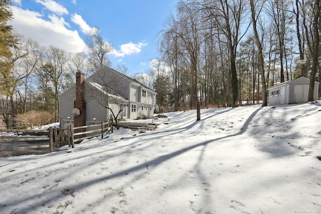 view of snow covered exterior featuring a garage, an outdoor structure, a chimney, and fence