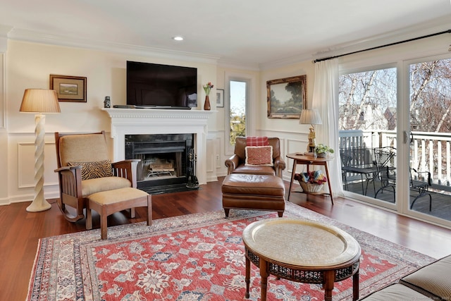 sitting room with wood finished floors, a decorative wall, a fireplace with flush hearth, and crown molding