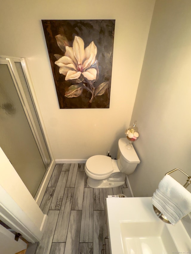 bathroom with toilet, wood finish floors, vanity, baseboards, and a stall shower