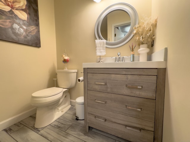 half bathroom featuring baseboards, vanity, toilet, and wood finished floors