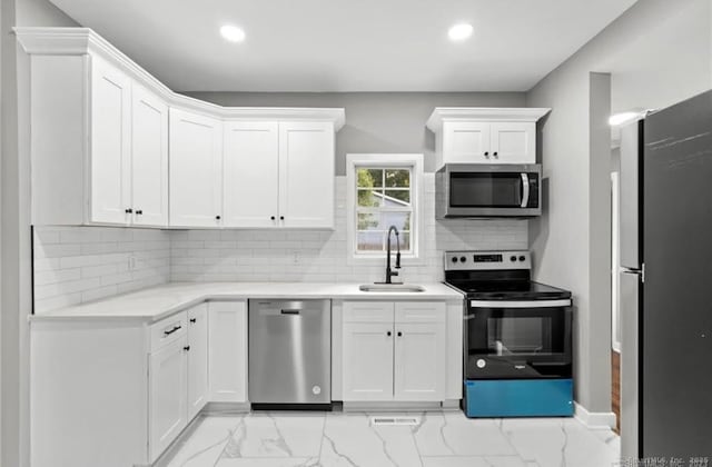 kitchen featuring marble finish floor, stainless steel appliances, white cabinetry, a sink, and recessed lighting