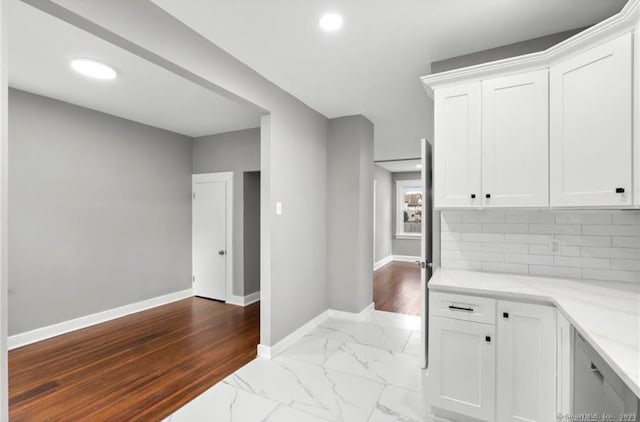 kitchen featuring light stone counters, white cabinets, baseboards, marble finish floor, and tasteful backsplash