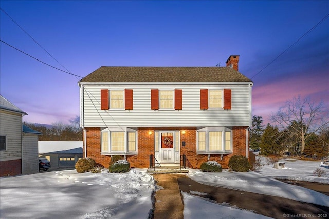 colonial-style house featuring a chimney and brick siding