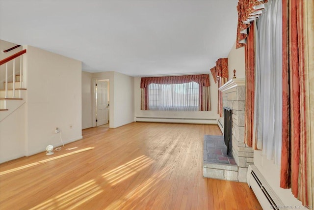 unfurnished living room featuring a baseboard radiator, stairs, a fireplace with raised hearth, and wood finished floors