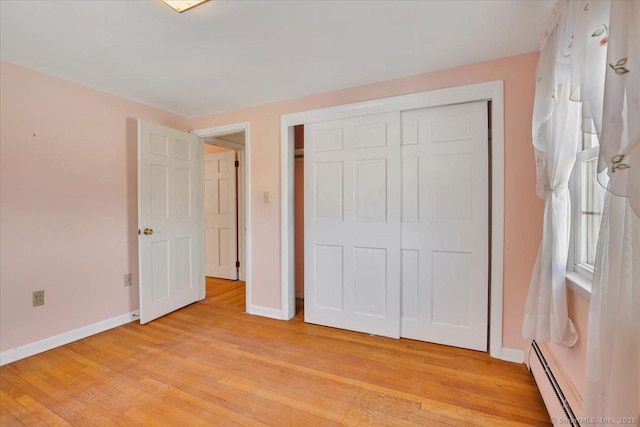 unfurnished bedroom with a baseboard heating unit, a closet, baseboards, and light wood-style floors