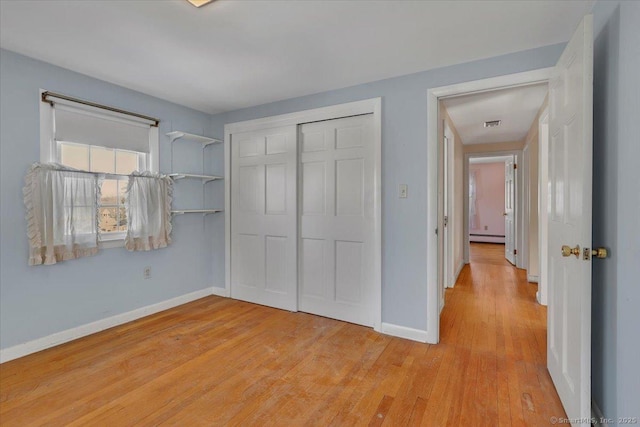 unfurnished bedroom with a baseboard heating unit, a closet, light wood-style floors, and baseboards