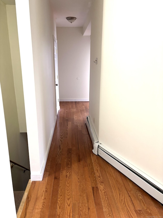 hallway featuring a baseboard heating unit, baseboards, and wood finished floors