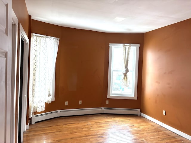 unfurnished room featuring a baseboard heating unit, light wood finished floors, and baseboards