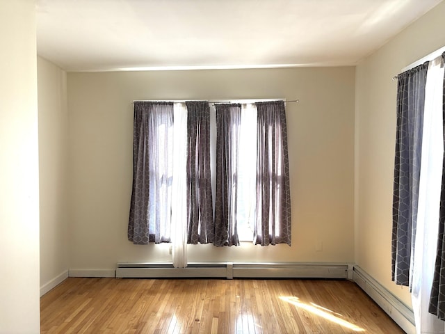 spare room with a baseboard radiator, hardwood / wood-style flooring, and baseboards