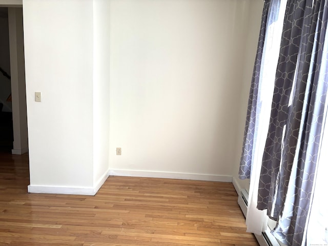 empty room with light wood-style floors, a baseboard radiator, and baseboards