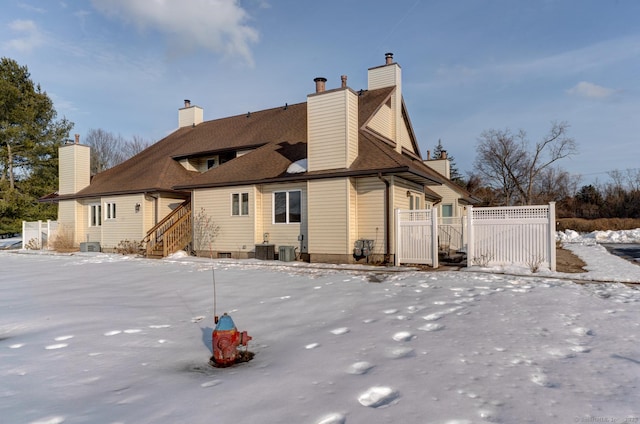 snow covered rear of property featuring a chimney, fence, central AC, and roof with shingles