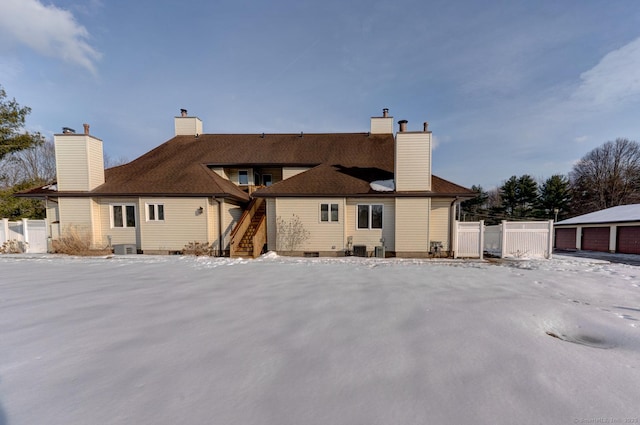 snow covered rear of property featuring central AC unit, a chimney, stairway, a detached garage, and fence