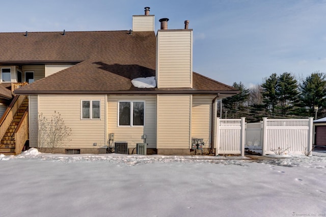 snow covered property featuring a shingled roof, a chimney, fence, and cooling unit