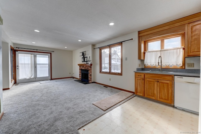 kitchen featuring brown cabinetry, dishwasher, dark countertops, a brick fireplace, and a sink