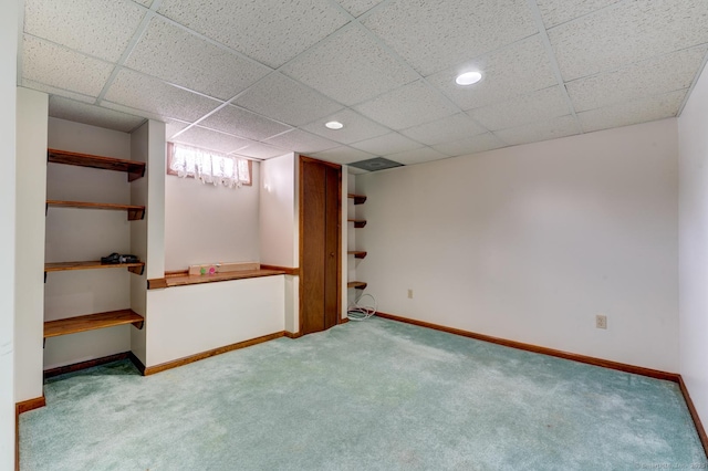 below grade area with light carpet, baseboards, and a drop ceiling