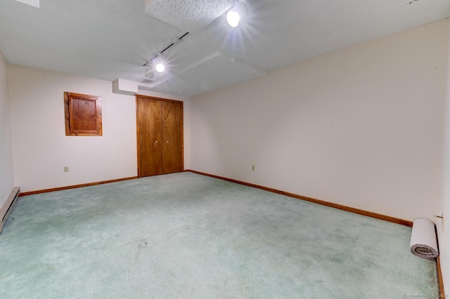 empty room featuring a textured ceiling, baseboards, track lighting, and light colored carpet